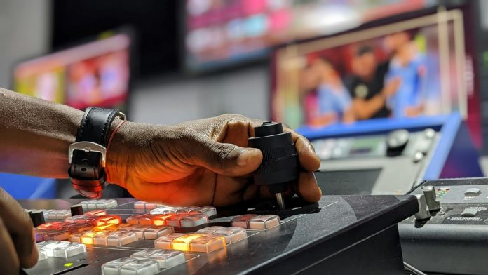Vizuális magyarázó: piacrész változása — A hand operates a broadcast control mixer in a television studio setting.