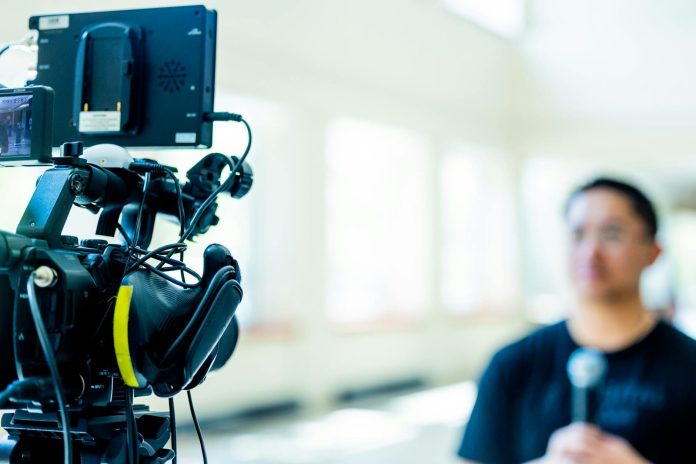 Podcast: értéklánc elemzés — Professional video camera setup focusing on an interview with blurred subject in