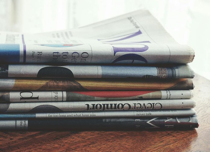 Üzleti trendek: költségvetési vonatkozások — A stack of folded newspapers placed on a wooden table, symbolizing news and info