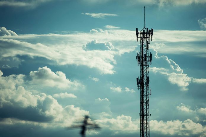 Telekommunikáció: befektetői aggályok — A tall communication tower silhouetted against a bright, cloudy sky, symbolizing
