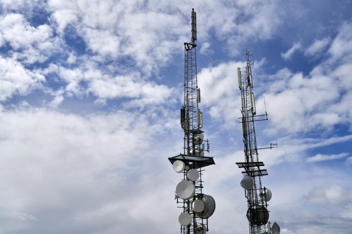 Mobilszolgáltatók monitor: OLAF-jelentések kontextusában — Telecommunication towers with antennas and dishes under a bright cloudy sky.