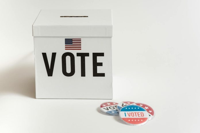 Pártpreferencia monitor: Visegrádi összehasonlítás — White ballot box with USA flag and 'I Voted' badges on a white background.