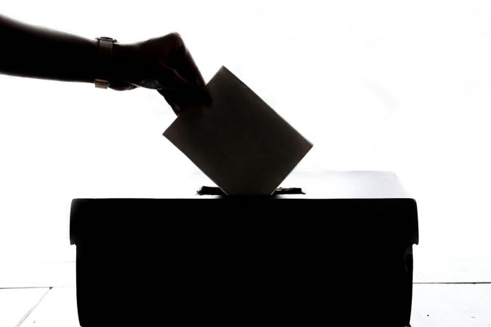 Közvélemény-kutatás: konszolidált adatok — Silhouette of a hand placing a vote into a ballot box, symbolizing democracy.