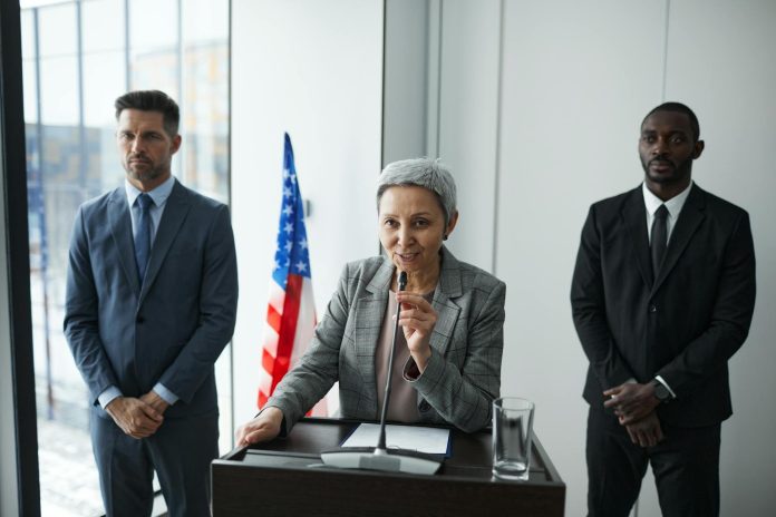 Mathias Corvinus Collegium (MCC) — KEKVA-vagyonvisszaszerzés folyamatban — A female politician delivers a speech with bodyguards and an American flag