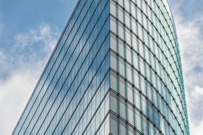 Állami ingatlan-portfólió átruházások — Tiborcz, Garancsi, Jellinek köre — A sleek glass skyscraper reflecting the blue sky and clouds, showcasing mod