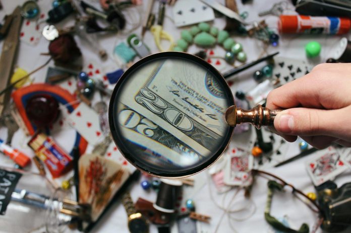 Direkt36 oknyomozás: 4iG titkos állami feltőkésítése a védelmi felvásárlások előtt — A hand holding a magnifying glass focusing on a twenty dollar bil